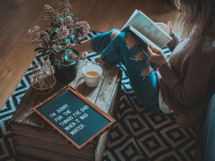 A woman in jeans reading a book in a cozy setting, a mug of tea by her side—embodying the truth that creativity and success can coexist, debunking the 'starving artist' myth.