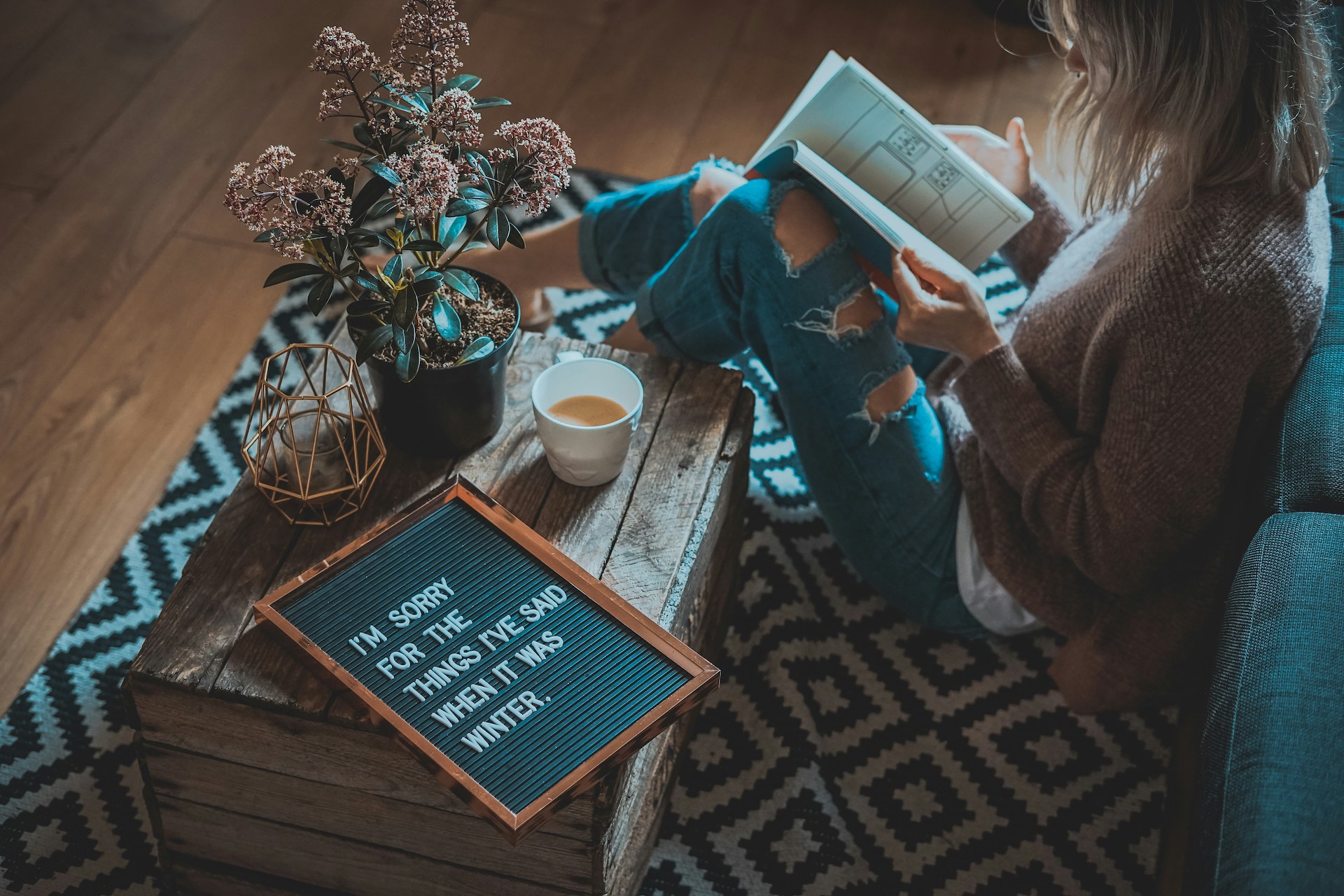 A woman in jeans reading a book in a cozy setting, a mug of tea by her side—embodying the truth that creativity and success can coexist, debunking the 'starving artist' myth.