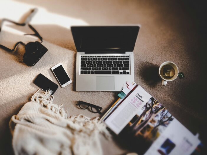 A laptop, phones, and a magazine scattered on a table, representing the hustle of managing multiple streams of income.