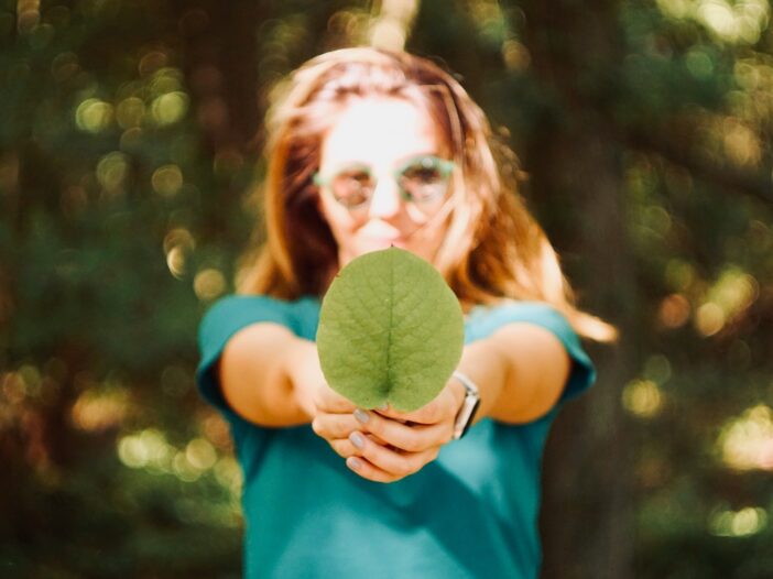 A woman holding up a leaf, reporting on climate impact as part of her environmental journalism.