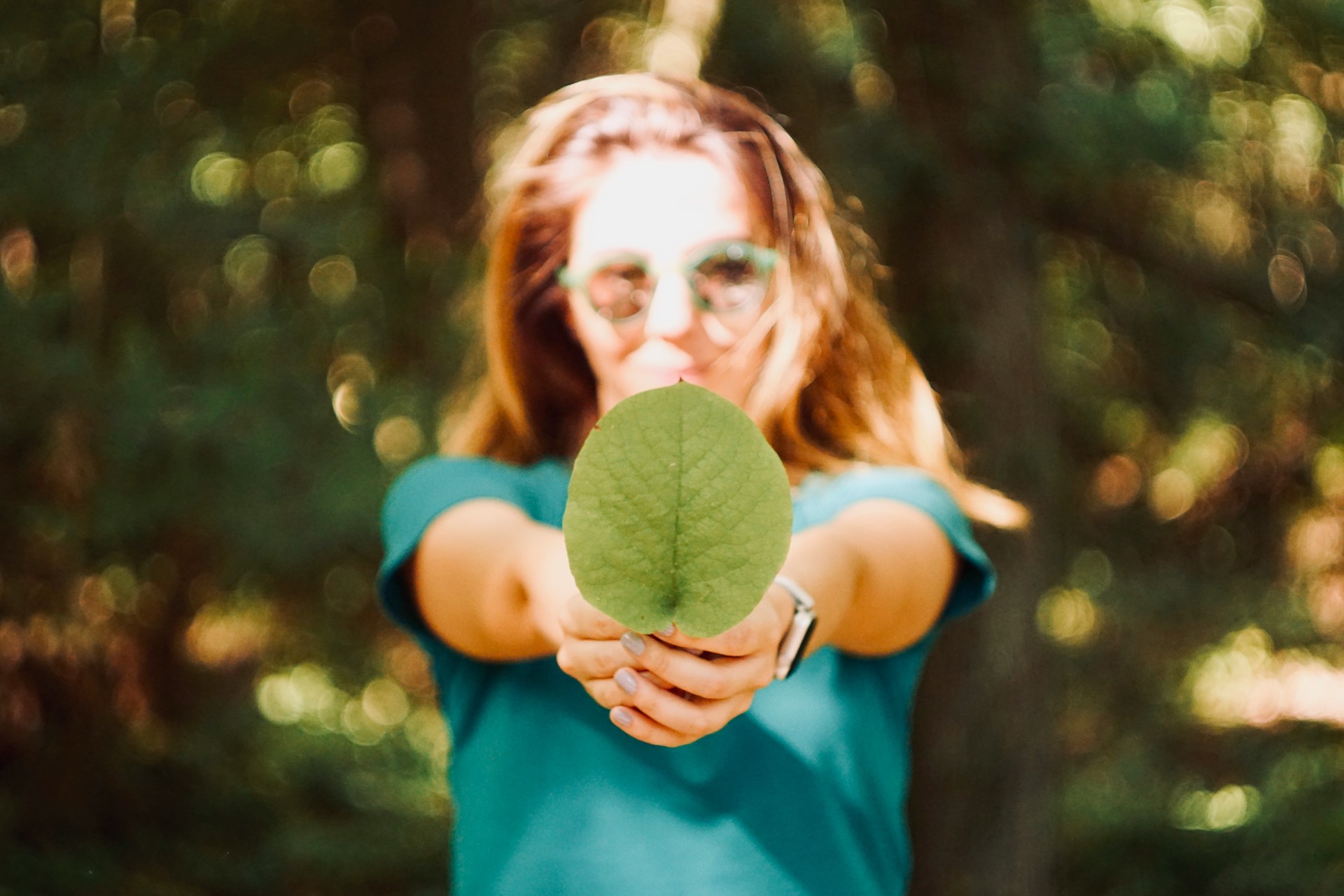 A woman holding up a leaf, reporting on climate impact as part of her environmental journalism.