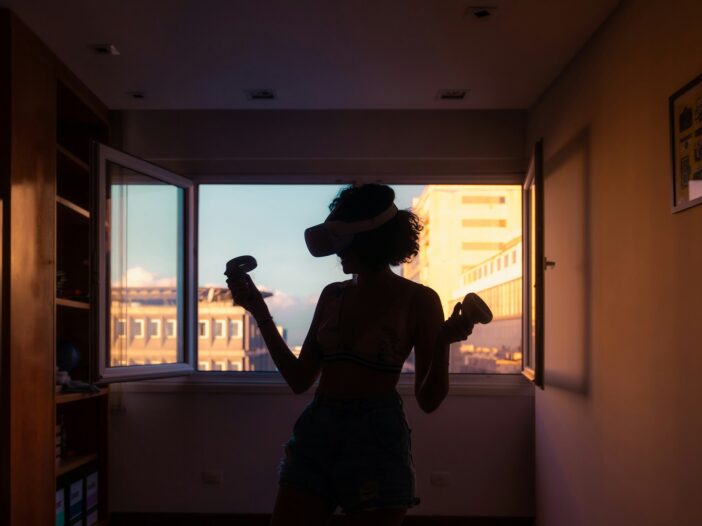 A woman standing by the window, wearing a VR headset, experiencing the virtual worlds that gaming journalism brings to life.