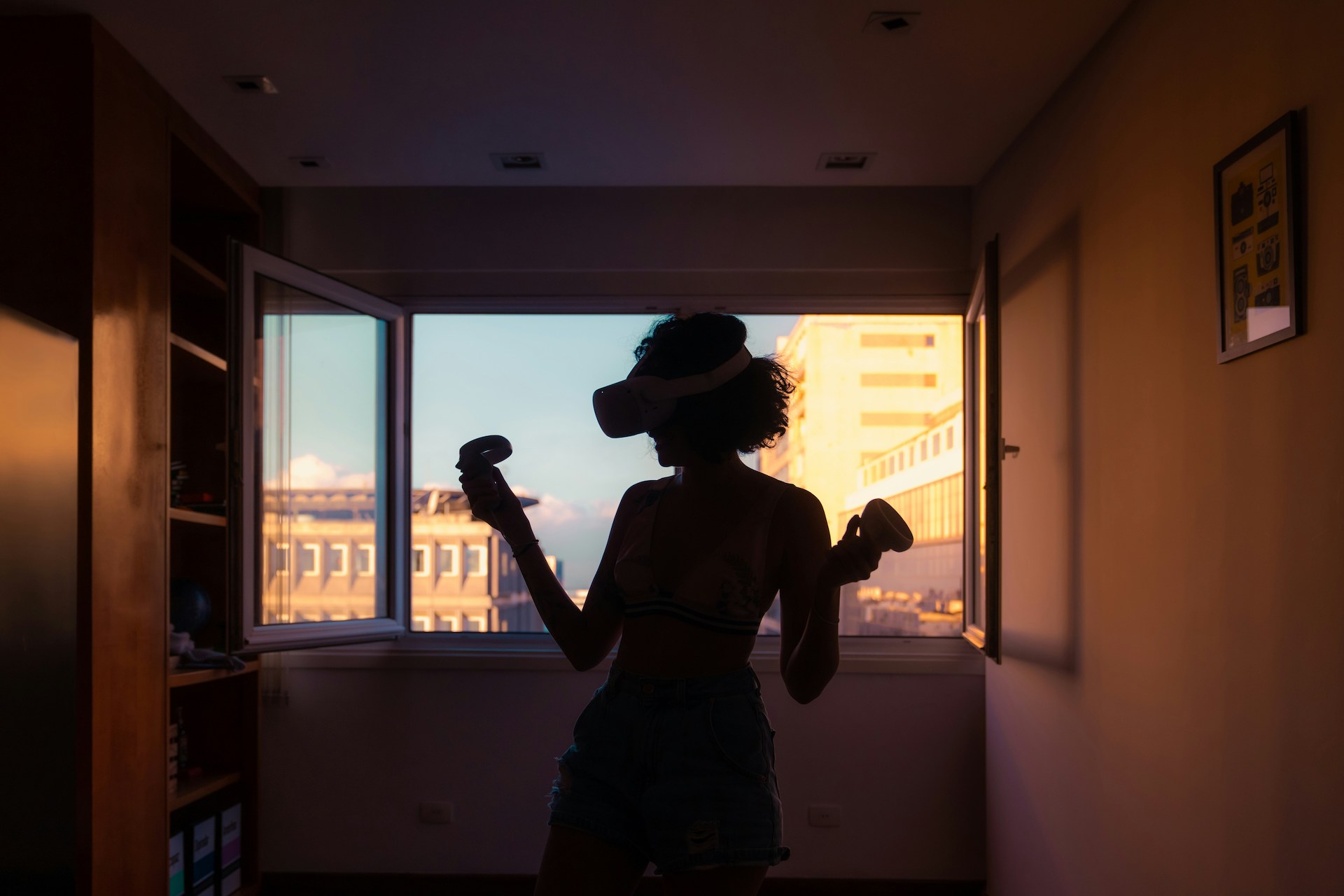 A woman standing by the window, wearing a VR headset, experiencing the virtual worlds that gaming journalism brings to life.