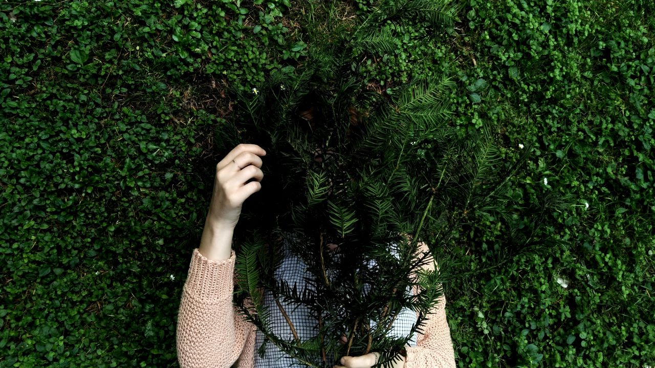 Visual metaphor for imposter syndrome—a person concealing themselves behind a leafy plant.